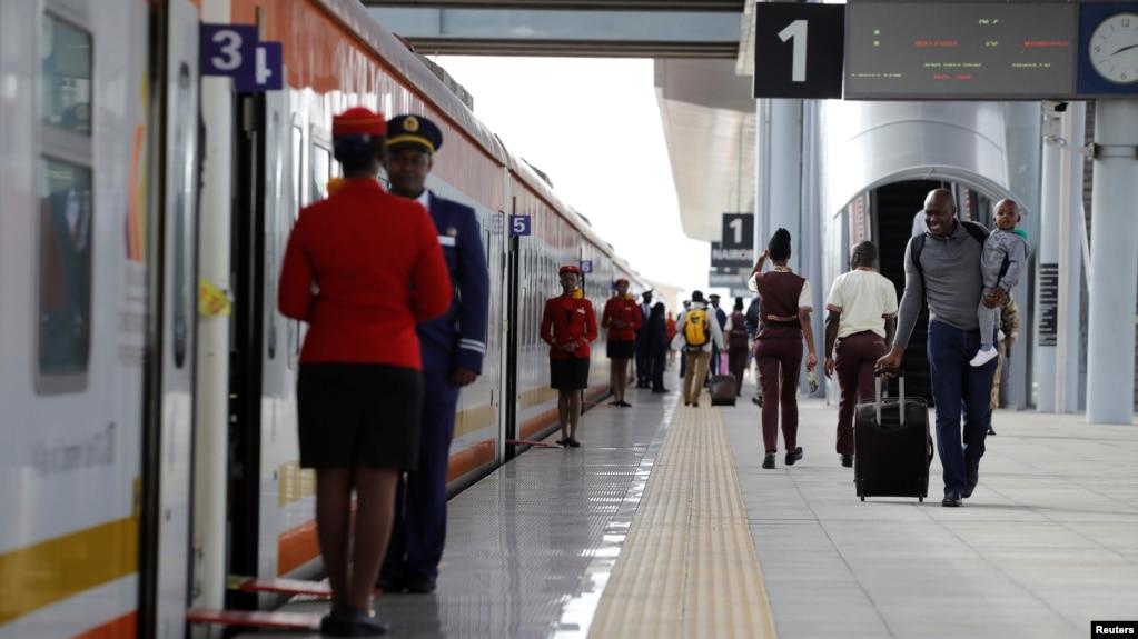 A man carries an infant as he walks along the platform in front an SGR train traveling to Mombasa from the Nairobi SGR Terminus, outside Nairobi, Kenya, October 22, 2019. Source: https://www.voanews.com/a/africa_cost-china-built-railway-haunts-kenya/6184880.html